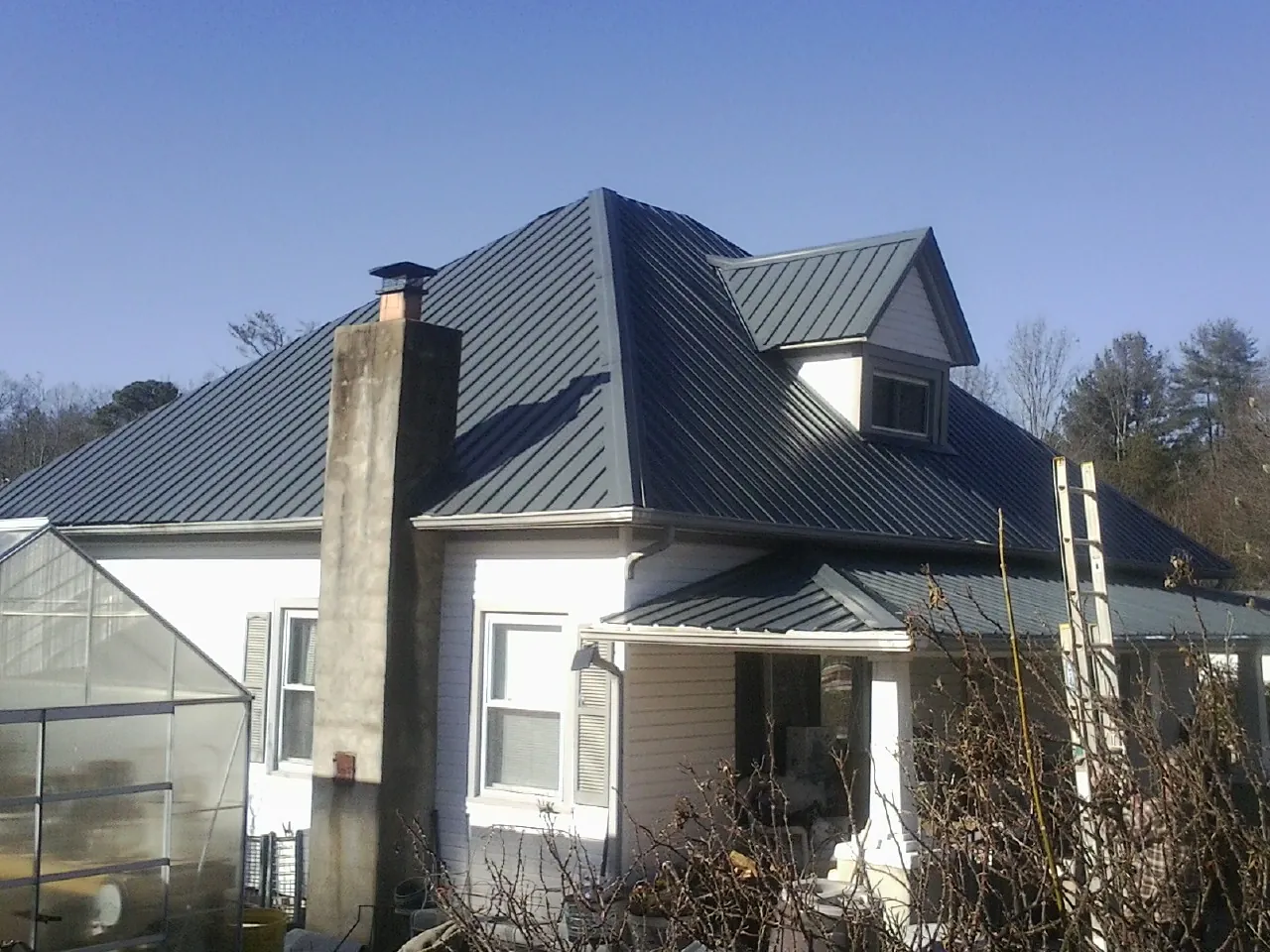 Dark blue standing seam metal roof on a white farmhouse with dormer — Slate & Tile Roof Repair by Roofing Brothers in Park Forest