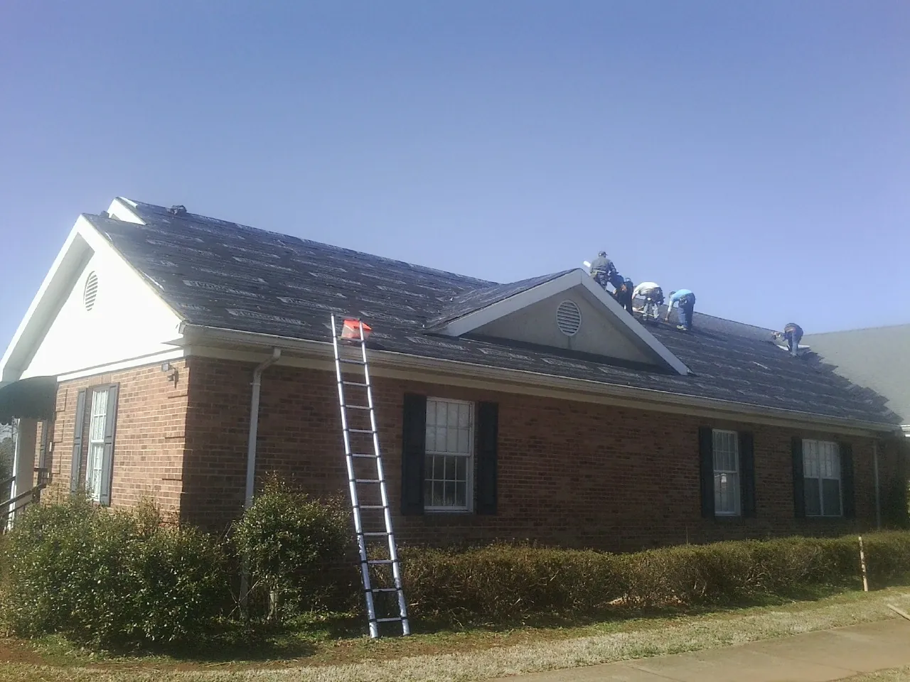 Crew tearing shingles off a brick ranch roof with a ladder set — Metal Roof Repair work by our crew in Park Forest
