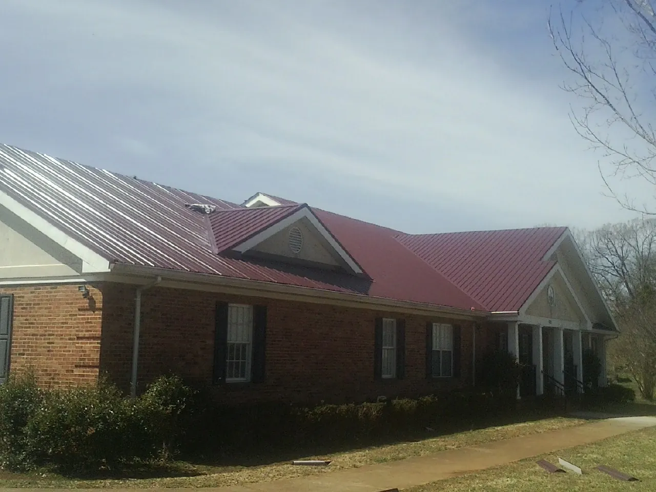 Red metal roof with gabled entries on a long brick building, from a Hail Damage Roof Repair job in Park Forest