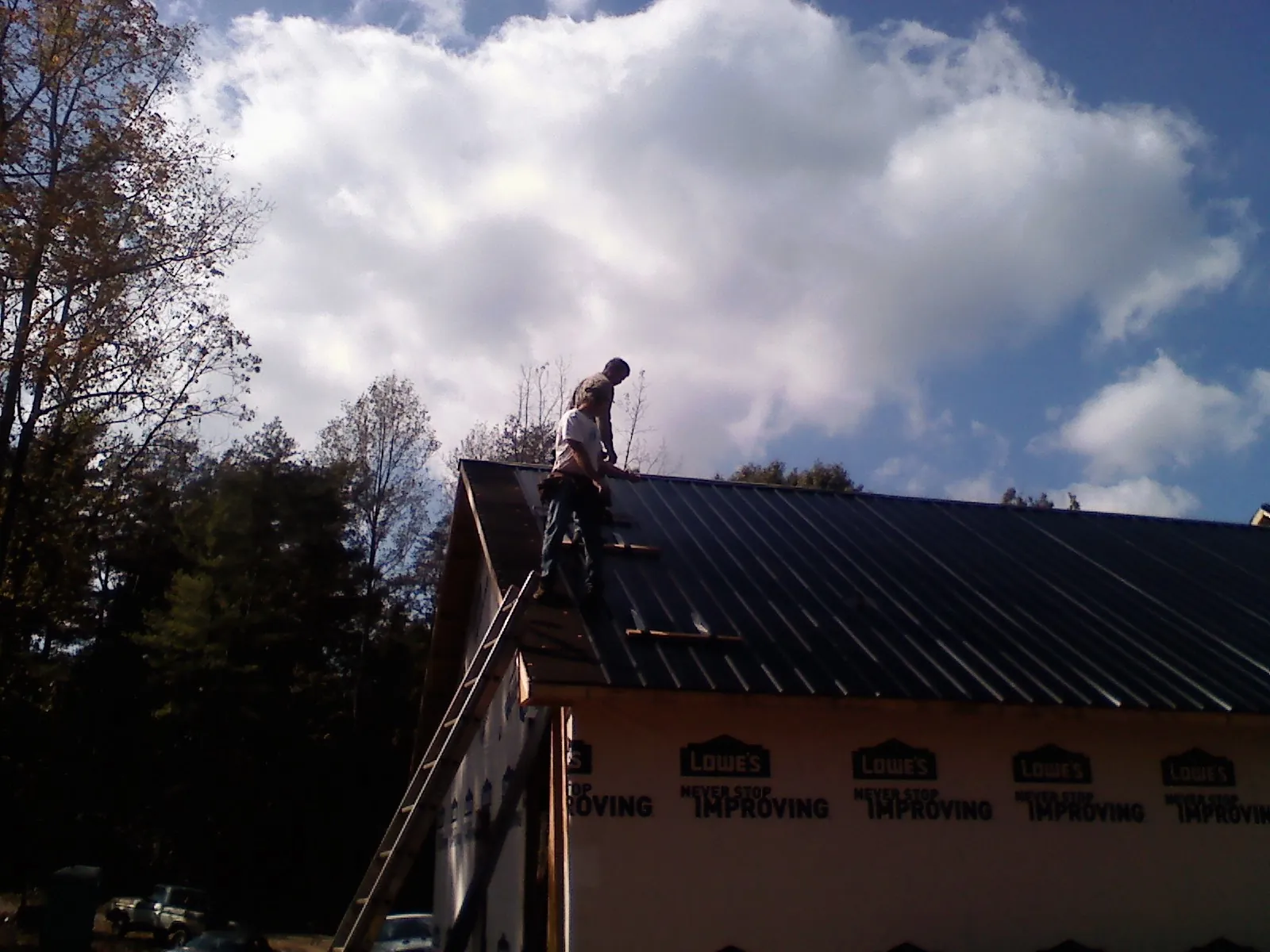 Roofer fastening dark metal panels high against a cloudy sky, from a Roof Inspection job in Park Forest