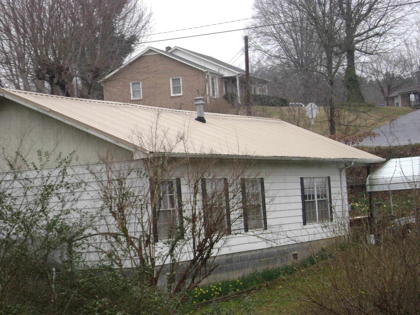 Tan metal roof on a white sided house set into a hillside — Commercial Roofing by Roofing Brothers in Park Forest